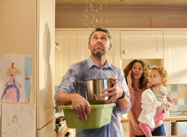 Family standing under a leaking roof with a bucket and calling contractor