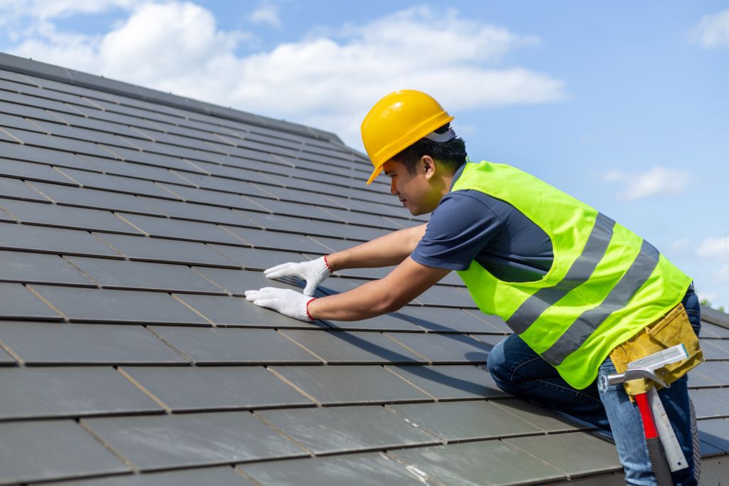 A Worker with White Gloves is Replacing Gray Tiles or Shingles on the House
