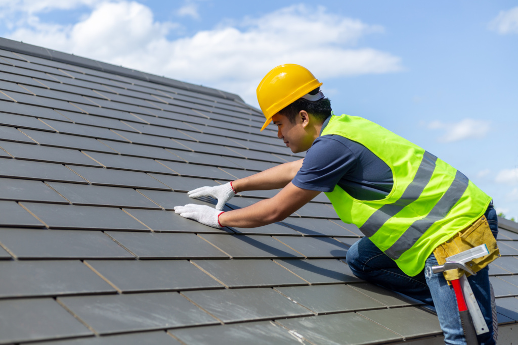 Roof repair, worker with white gloves replacing gray tiles or shingles on house with blue sky as background and copy space, Roofing